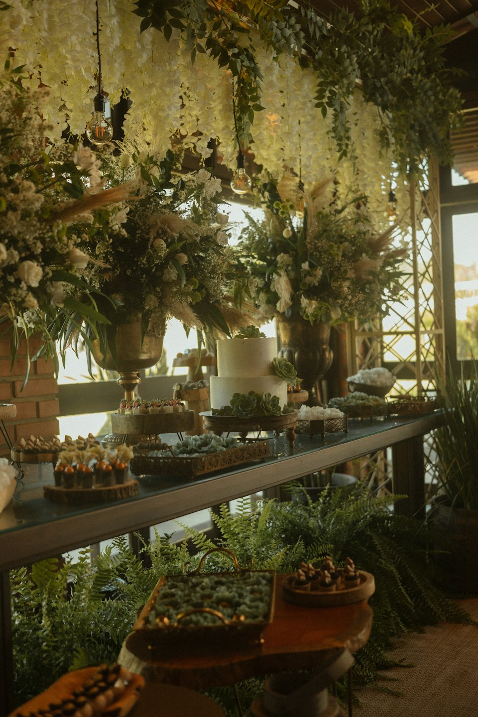Dessert table with cake, sweets, and abundant floral arrangements.